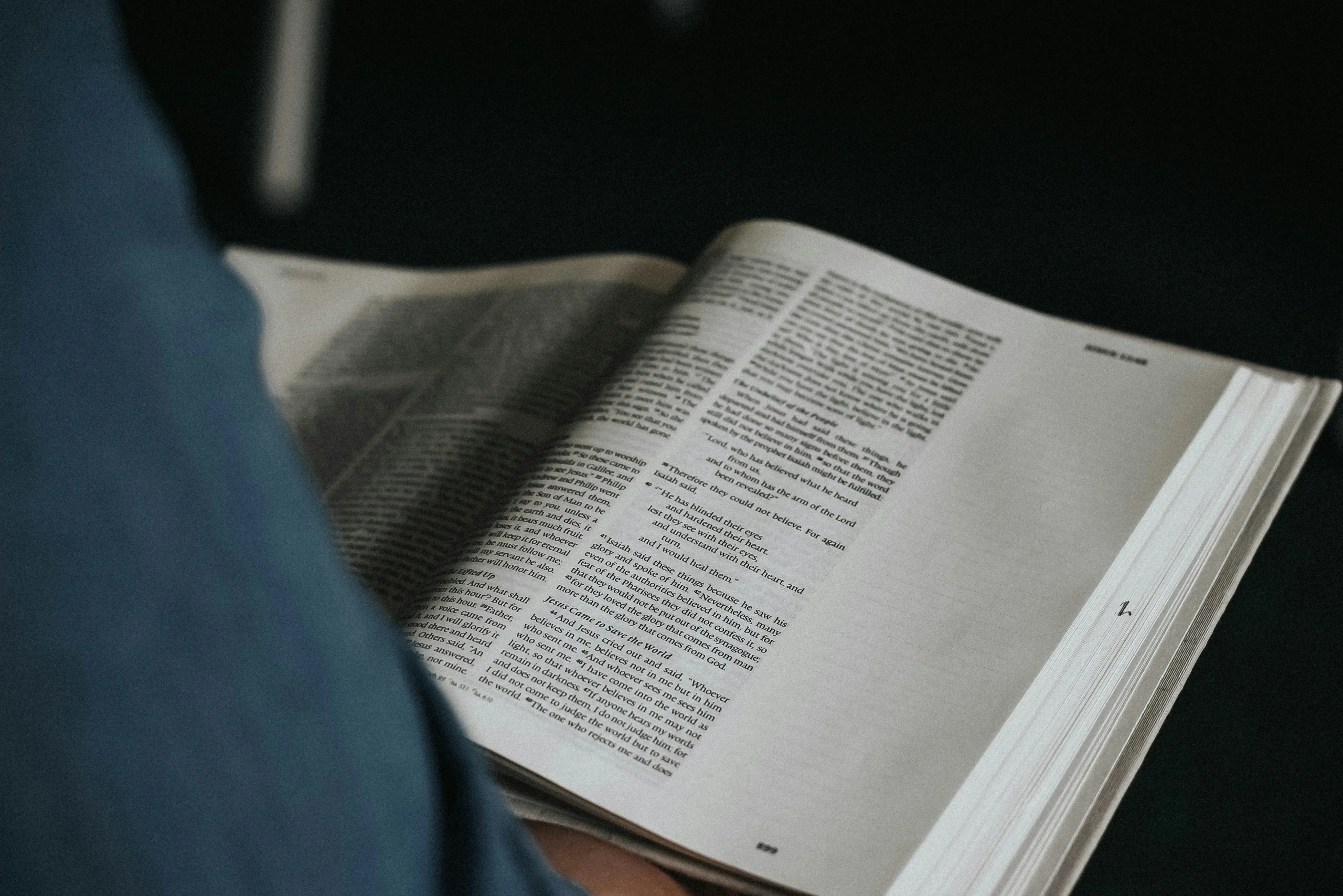 man holding open Bible. Bible is open to Isaiah. Photo by Adrian Ordonez on Unsplash